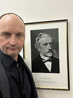 Dr. Christian Hoeckle vor einem schwarz-weiß Porträt von Bernhard von Langenbeck