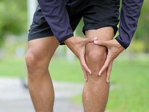Ein Mann in Joggingklamotten hält sich das linke Knie.