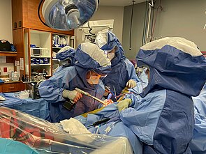 Zwei Ärzte in blauer Schutzkleidung im OP-Saal mit Operationsbesteck in der Hand.