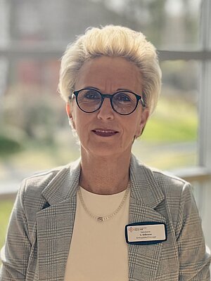 Porträt von Claudia Süßman, einer Frau mittlerenAlter smit blonden Kurzhaarschnitt und Brille, die als Sekretärin der Orthopädie im Cellitinnen-Krankenhaus Maria-Hilf in Bergheim arbeitet