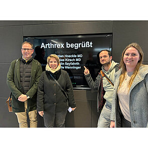 Arthrex Vier Personen vor einem Bildschirm, der sie im Arhro-Lab willkommen heißt.