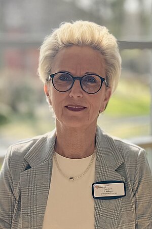 Porträt von Claudia Süßman, einer Frau mittlerenAlter smit blonden Kurzhaarschnitt und Brille, die als Sekretärin der Orthopädie im Cellitinnen-Krankenhaus Maria-Hilf in Bergheim arbeitet