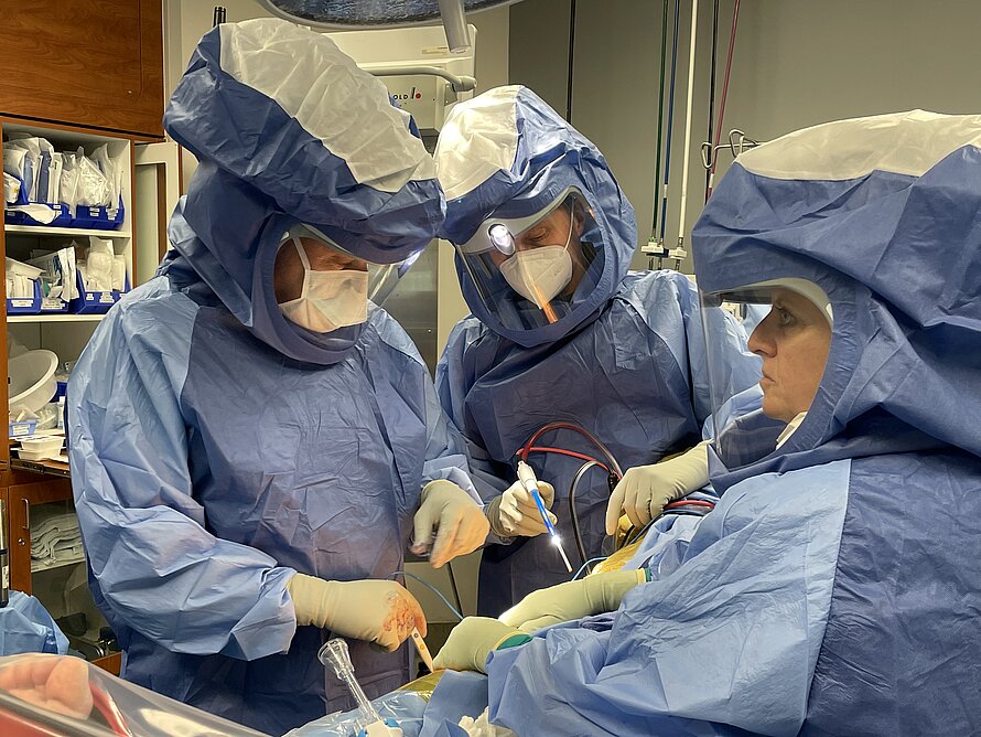 Zwei Ärzte in blauer Schutzkleidung im OP-Saal mit Operationsbesteck in der Hand.