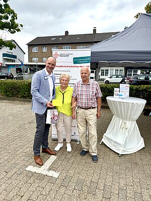 Arzt mit einem älteren Ehepaar auf einem Marktstand