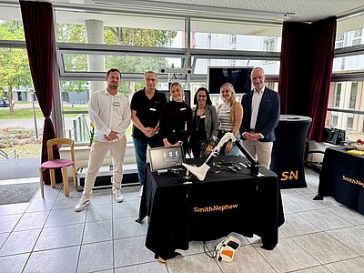 Team Orthopädie und Smith and Nephew Sechs Menschen, drei Männer und drei Frauen, stehen hinter einem Tisch auf dem das CORI System aufgebaut ist .